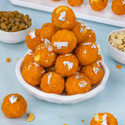 Orangish-brown sweet balls with white toppings on a white plate, surrounded by bowls of nuts and raisins on a light blue background.
